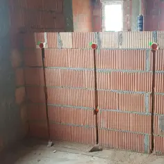 Ściana z pustaków ceramicznych z wyżłobieniami pod kable i widocznymi puszkami instalacyjnymi.