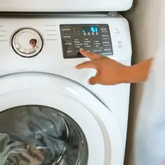 Ręka naciska przyciski na pralce Samsung, pokazując jak zresetować pralkę.