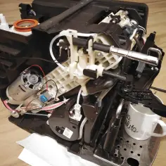 Rozłożony ekspres DeLonghi, który nie spienia mleka. Widoczne elementy mechanizmu, silnik i przewody.