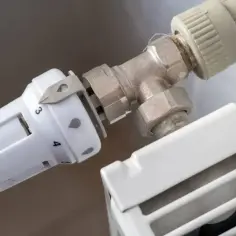 Wymiana termostatu w grzejniku bez spuszczania wody. Widoczny biały termostat z oznaczeniami temperatury i metalowy zawór.