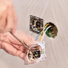 Instalator podłącza włącznik światła podwójny trzy przewody. Widać rękę z wkrętakiem i mechanizm włącznika.