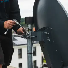 Instalator dokręca śruby, pokazując, jak ustawić antenę satelitarną.
