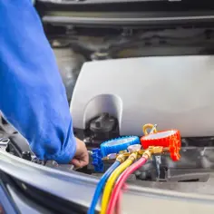 Mechanik z manometrami pod maską samochodu. Czas nabijania klimatyzacji zależy od wielu czynników.
