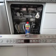 Zmywarka Bosch z otwartymi drzwiczkami, w środku naczynia i butelka środka do czyszczenia zmywarki Kret.