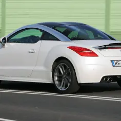 Biały Peugeot RCZ z czarnym dachem pędzi po drodze, za zielonym ekranem dźwiękochłonnym.