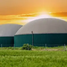 Dwa zielone zbiorniki z kopułami na tle zachodzącego słońca. To instalacja do produkcji biogazu, który po oczyszczeniu staje się biometanem.