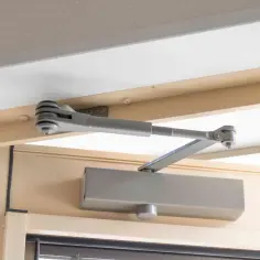 Mechanizm samozamykacza drzwi zamontowany na futrynie. Umożliwia płynną regulację samozamykacza drzwi, zapewniając komfort użytkowania.