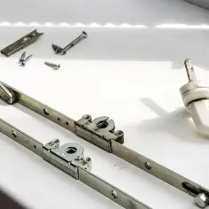 Rozłożony uszkodzony mechanizm okna uchylnego i klamka.