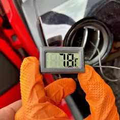 Rękawiczki w kolorze pomarańczowym trzymają termometr pokazujący 78°F. To część samodzielnego nabijania klimatyzacji.
