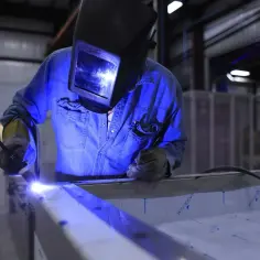 Spawanie aluminium migomatem. Pracownik w masce spawalniczej łączy elementy metalowe, tworząc jasny łuk świetlny.