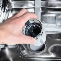Dłoń wyjmuje filtr zmywarki, który może być przyczyną, że zmywarka nie domywa naczyń.