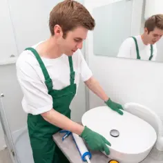 Fachowiec w zielonym ogrodniczkach montuje umywalkę. Sprawdź montaż umywalki cena i jakość wykonania.