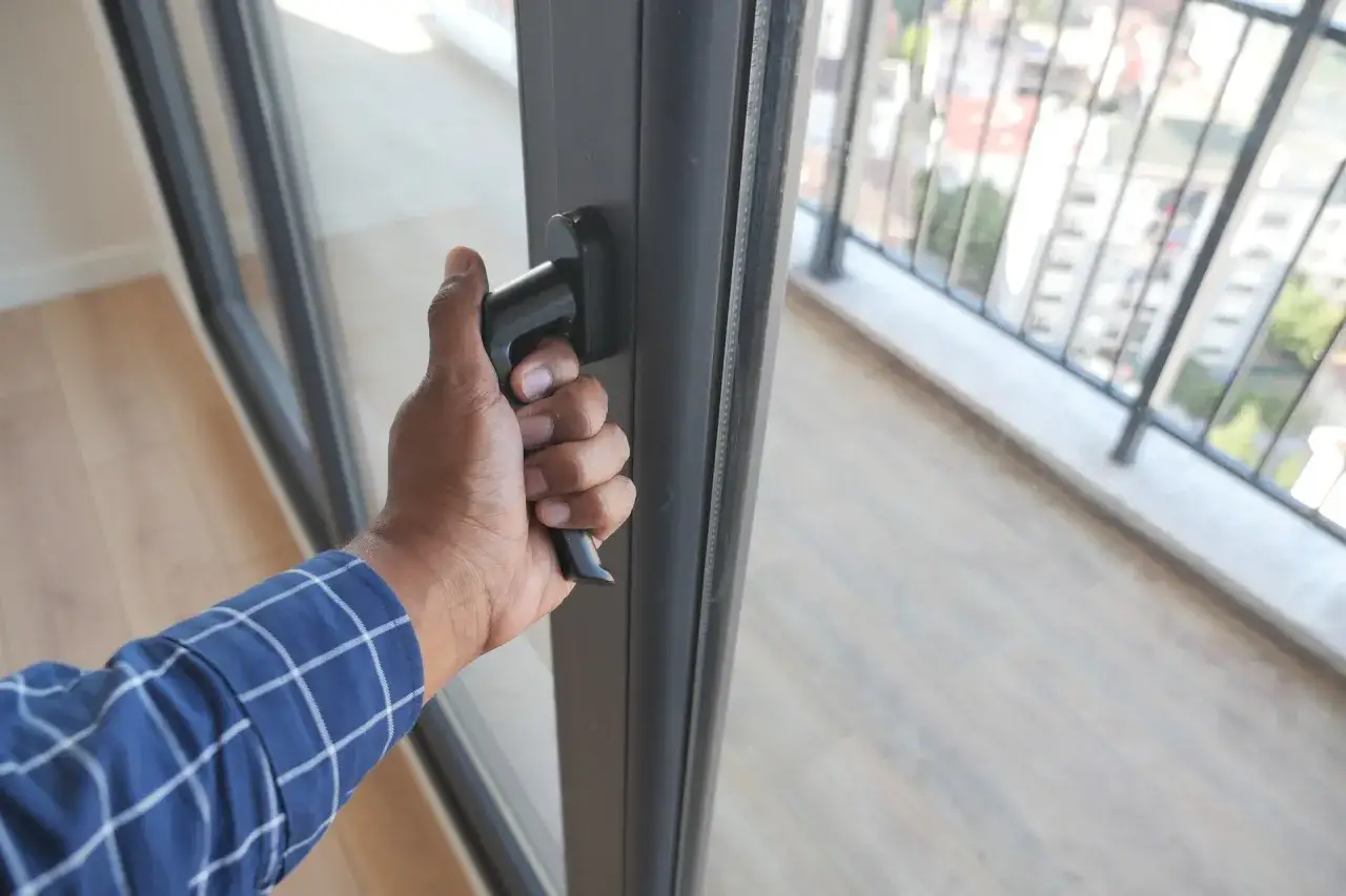 Dłoń chwyta za klamkę, regulacja drzwi balkonowych uchylnych. Widok na balkon i miasto.