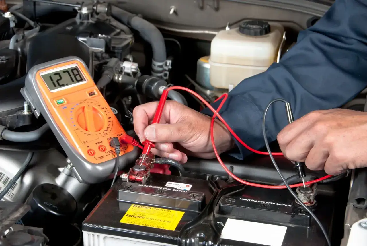 Mechanik sprawdza napięcie akumulatora multimetrem. Wynik 12.78V sugeruje, że akumulator nie jest rozładowany.