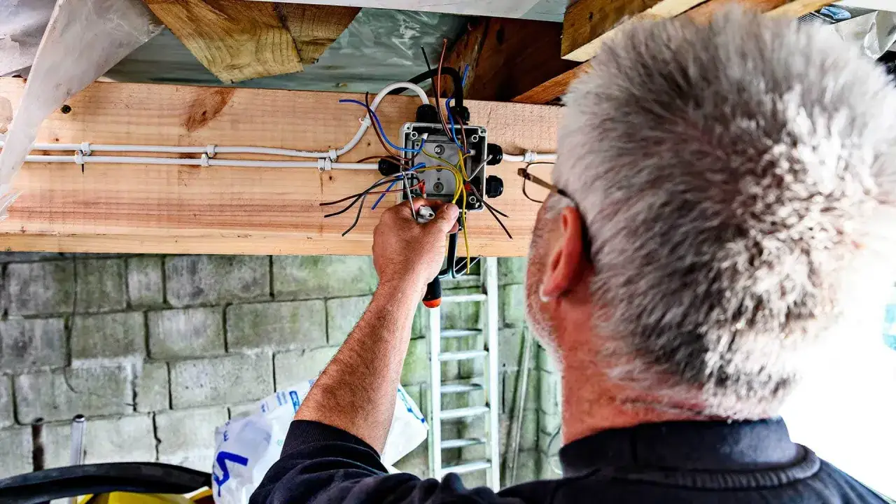 Elektryk wykonuje przegląd instalacji elektrycznej, łącząc przewody w puszce.