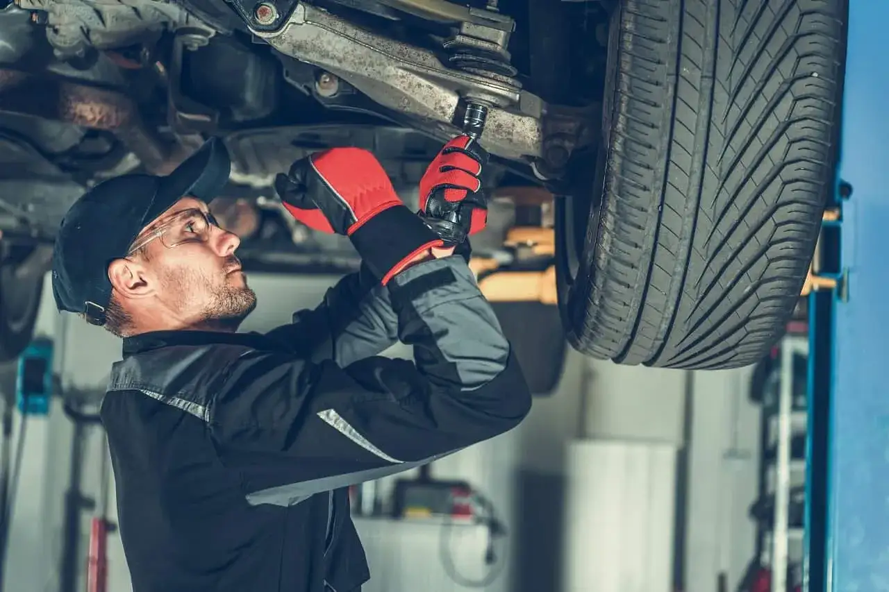 Mechanik w rękawicach dokonuje wymiany sworznia wahacza w podniesionym samochodzie.
