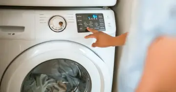 Ręka naciska przyciski na pralce Samsung, pokazując jak zresetować pralkę.