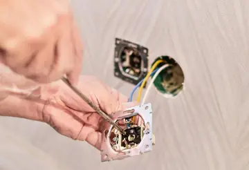 Instalator podłącza włącznik światła podwójny trzy przewody. Widać rękę z wkrętakiem i mechanizm włącznika.
